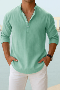 Man wearing a light green long-sleeve shirt and white pants against a light blue background
